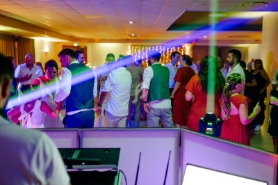 Des personnes dansent dans une salle éclairée par des lumières colorées, avec un DJ en arrière-plan.