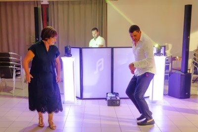 Deux personnes dansent sur une piste éclairée, avec un DJ en arrière-plan devant son équipement.