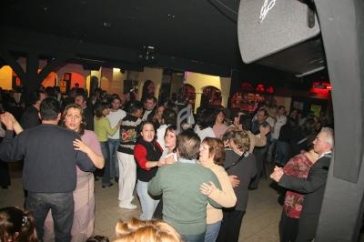 Des personnes dansent en couple dans une salle animée avec éclairage tamisé et un bar en arrière-plan.