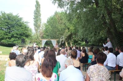 Cérémonie en plein air avec des invités assis, un officiant et un couple sous une arche décorée, entourés de verdure.