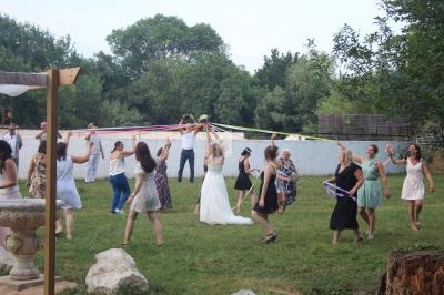 Des personnes dansent en cercle autour d'une mariée tenant des rubans colorés dans un jardin verdoyant.