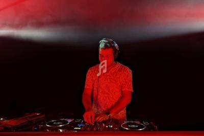 Un DJ mixant de la musique sur une table de mixage, éclairé par des lumières rouges dans un environnement sombre.