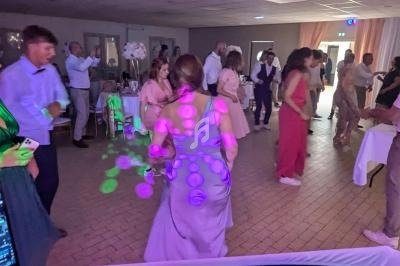Des invités dansent dans une salle éclairée par des lumières colorées lors d'une fête ou d'un événement festif.