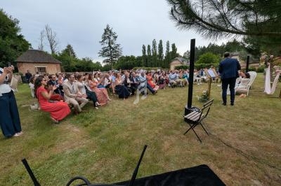 Un groupe de personnes assises en extérieur lors d'une cérémonie, avec un musicien jouant devant eux.