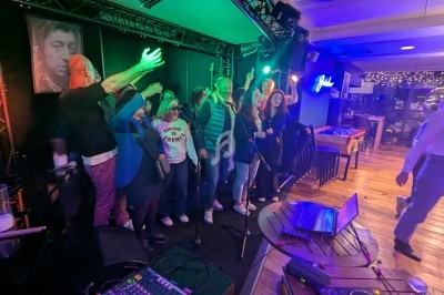 Des personnes chantent ensemble sur une scène éclairée, entourées de lumières colorées dans un espace intérieur animé.