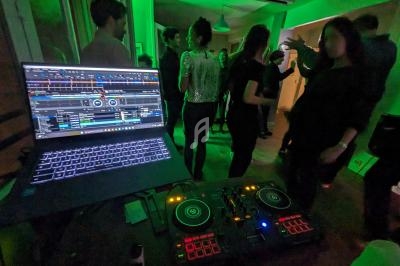 Personnes dansant dans une pièce éclairée de lumières vertes, avec une table de mixage et un ordinateur au premier plan.