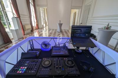 Poste de DJ avec platines, table de mixage, ordinateur portable et casque dans une salle lumineuse au sol carrelé.