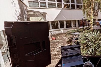 Ordinateur portable et enceinte installés dans une cour extérieure entourée de végétation et de bâtiments modernes.