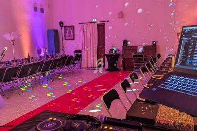 Salle décorée pour un événement avec tables alignées, éclairages colorés et matériel de DJ au premier plan.