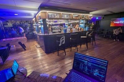 Bar moderne avec comptoir éclairé, tables, baby-foot, écran mural et ambiance tamisée.