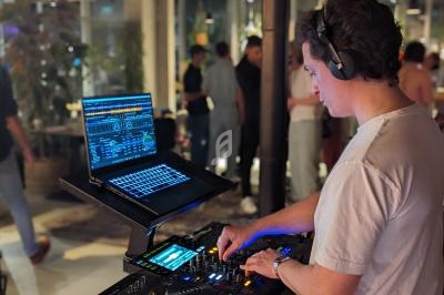 Un DJ mixe de la musique sur une console avec un ordinateur portable, dans un espace intérieur animé.