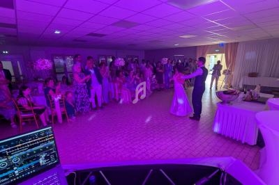 Un couple danse au centre d'une salle éclairée de lumières violettes, entouré d'invités attentifs.