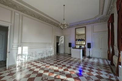 Salle lumineuse avec sol en carreaux rouges et blancs, moulures au plafond, lustre, tables, chaises et équipement audio.