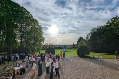 Groupe de personnes rassemblées dans une cour extérieure, entourée de verdure, sous un ciel partiellement nuageux.