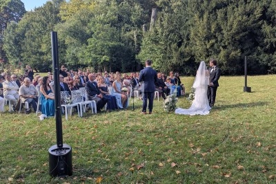 Cérémonie de mariage en plein air avec un couple devant des invités assis sur des chaises, entourés de verdure.