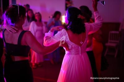Des invités dansent lors d'une soirée, une mariée en robe blanche au centre sous des lumières colorées.