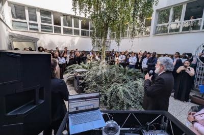 Un homme s'exprime devant un public rassemblé dans une cour extérieure entourée de bâtiments modernes.