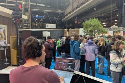 Un DJ mixe sur son ordinateur portable lors d'un événement, face à un public rassemblé dans un espace intérieur.
