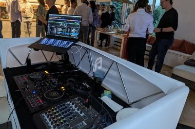 Console de DJ en premier plan avec des invités discutant dans un salon moderne en arrière-plan.