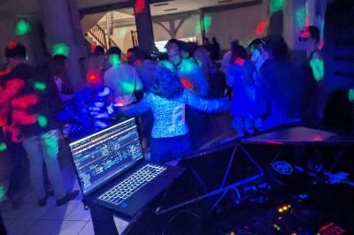Personnes dansant sous des lumières colorées dans une salle, avec une table de mixage et un ordinateur au premier plan.