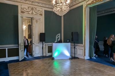 Salle élégante avec parquet, murs verts, moulures dorées, lustre central et espace aménagé pour une animation.