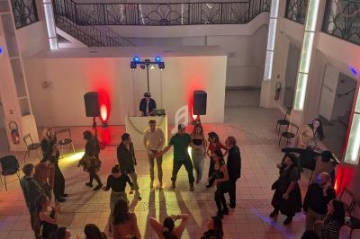 Groupe de personnes dansant dans une salle lumineuse avec un DJ en arrière-plan et des éclairages colorés.