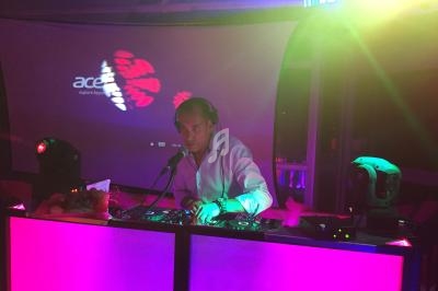 Un DJ mixe de la musique sur une table lumineuse dans une ambiance colorée et tamisée.