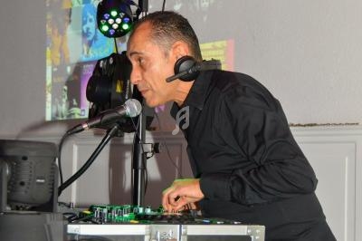 Un DJ mixe de la musique sur une console, avec des lumières colorées et des affiches en arrière-plan.