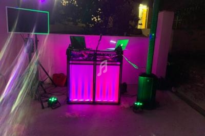 Poste de DJ éclairé par des lumières colorées, avec des équipements audio et visuels en extérieur.