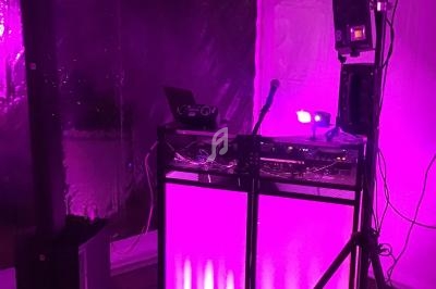 Équipement de DJ avec éclairage violet, comprenant une table de mixage, des haut-parleurs et des projecteurs.