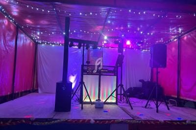 Scène de DJ éclairée par des lumières colorées, avec une table de mixage et des enceintes sous un chapiteau rouge.