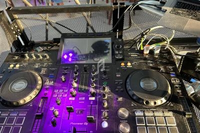 Table de mixage DJ avec platines, écran central et câblages, installée en extérieur sur une surface métallique.
