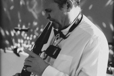 Un musicien en chemise blanche joue d'un instrument à vent électronique dans une ambiance lumineuse tamisée.