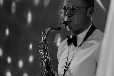 Un musicien en chemise et nœud papillon joue du saxophone dans une ambiance éclairée de lumières tamisées.