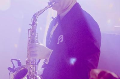 Un musicien en smoking joue du saxophone dans une ambiance lumineuse tamisée.