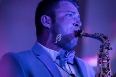 Homme en costume jouant du saxophone sous un éclairage violet.