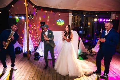 Un groupe de personnes, dont une mariée, danse et joue de la musique sur une scène éclairée lors d'une fête.