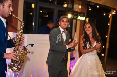 Un saxophoniste joue lors d'une fête, tandis qu'un homme et une femme applaudissent sur une piste éclairée.
