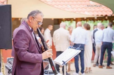 Un musicien joue de la flûte électronique lors d'un événement en extérieur, avec des invités en arrière-plan flou.