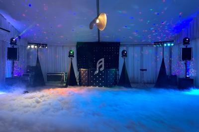 Salle de réception avec éclairage coloré, effets de fumée au sol et équipement de sonorisation installé.