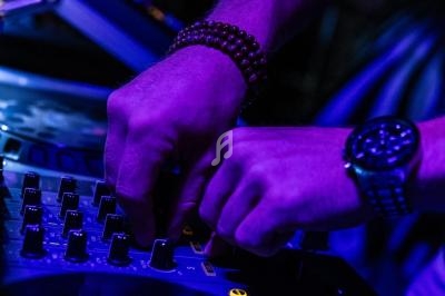Mains ajustant des boutons sur une table de mixage sous un éclairage violet.