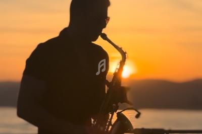 Silhouette d'un musicien jouant du saxophone au coucher du soleil, avec un paysage de collines en arrière-plan.