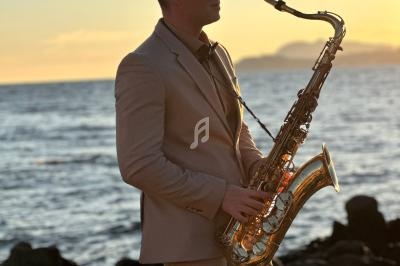 Un homme en costume joue du saxophone au bord de la mer au coucher du soleil.