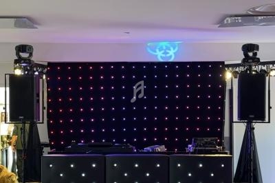 Configuration d'une scène avec une table de mixage, des enceintes et un fond lumineux à LED dans une salle.