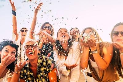 Un groupe de personnes souriantes lance des confettis en l'air dans une ambiance festive en extérieur.