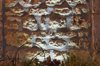 Mur en pierre éclairé par une lumière chaude, avec des fleurs colorées au premier plan.