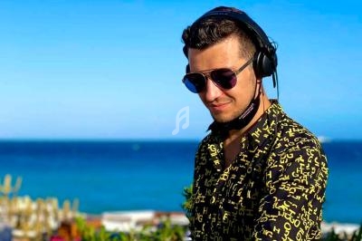 Un DJ portant un casque audio et des lunettes de soleil mixe en extérieur avec la mer en arrière-plan.
