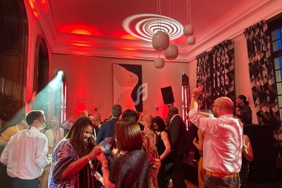 Des personnes dansent dans une salle éclairée par des lumières rouges, avec un DJ en arrière-plan.