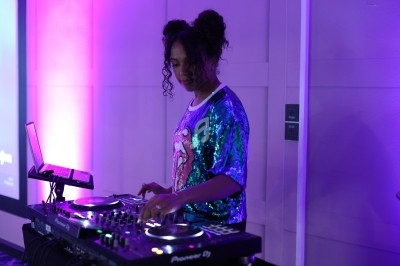 Une DJ mixe de la musique sur une console dans une pièce éclairée par des lumières violettes.