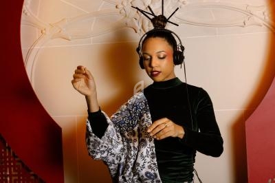 Femme portant un casque audio, dansant avec élégance devant un décor intérieur orné et lumineux.